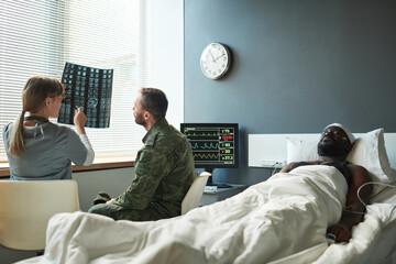 Young doctor explaining details of brain scan of injured patient to soldier in military uniform...