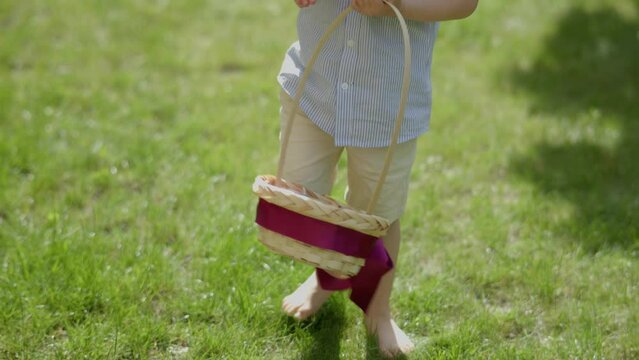 Easter egg hunt: barefoot child searching colorful Easter eggs hidden in grass. Boy kid picking Easter egg from ground put it into basket. Happy Easter celebration children activities outdoors