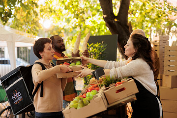 From farm to doorstep. Young girl courier wearing delivery bag picking up order at food market, delivering healthy fresh eco organic produce fruits and vegetables produced by local farmers