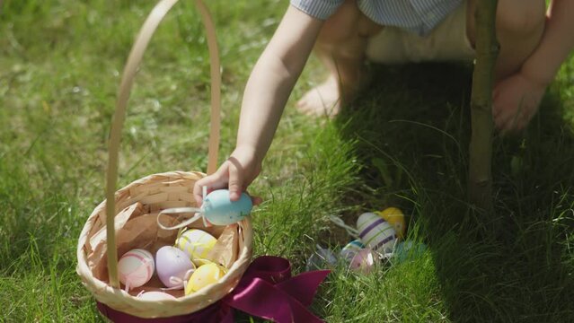 little child's hands picking up Easter eggs put them into basket outdoors. Easter egg hidden in green grass warm sunny spring daytime. Traditional Egg Hunt game for children