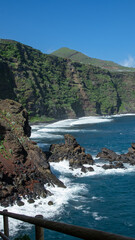 Playa de arena negra natural bajo un acantilado.