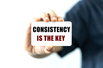 Consistency is the key text on blank business card being held by a woman's hand with blurred background. Business concept about consistency as a key of success.