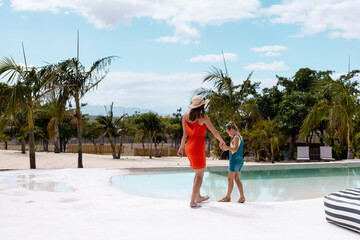 Happy biracial mother and daughter walking and holding hands by the swimming pool
