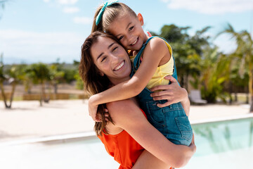 Fototapeta na wymiar Portrait of happy biracial mother and daughter embracing by the swimming pool