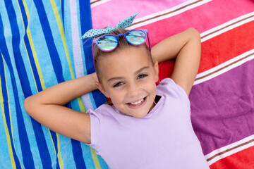 Portrait of happy biracial girl smiling and lying on towel by the swimming pool - obrazy, fototapety, plakaty