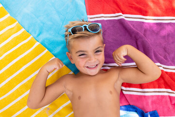 Portrait of happy biracial boy smiling and lying on towel by the swimming pool - obrazy, fototapety, plakaty