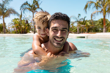 Portrait of happy biracial father and son playing together in swimming pool