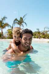Portrait of happy biracial father and son playing together in swimming pool - obrazy, fototapety, plakaty