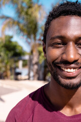Portrait of happy african american man looking at camera and smiling at beach, with copy space