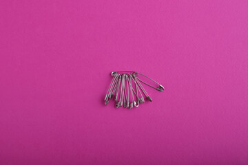 On a large bright pink textured background is a bunch of silver safety pins in various sizes and shapes. Sewing accessories. Copy space view