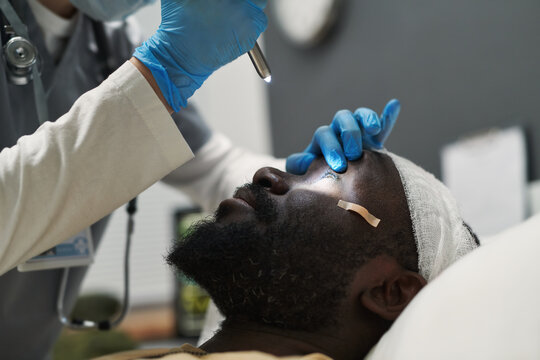 Close-up Of Doctor Or Nurse Opening Eye Of Injured Patient While Directing Light There While Checking Pupil Reaction During Examination