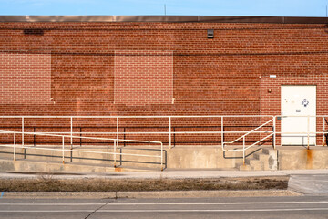 A landscape view of an orange brick wall of an industrial building with barricaded windows at sunset