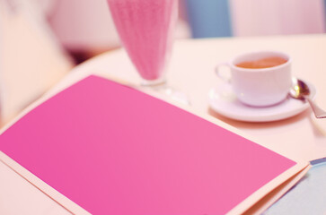 A bar table with a menu, a cup of coffee and a glass of pink shake