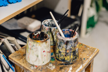 Artist water pots with paintbrushes on rustic school in classroom art studio 