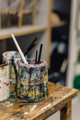 Artist water pots with paintbrushes on rustic school in classroom art studio 