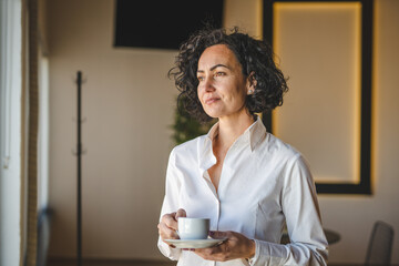 Mature woman having cup of coffee at home or office in morning