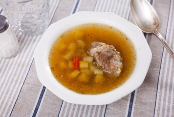 Fresh portion of meat soup with chopped potatoes and carrot served in bowl.