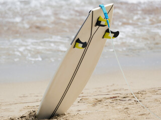 Professional short surfboard with fins in sand next the ocean.