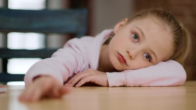 Boring mood. Cute upset little girl feeling bored and indifferent, lying on table and tapping with fingers, close up