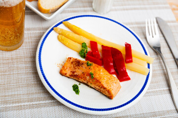 Porion of salmon fillet with white asparagus and red pepper served on table.