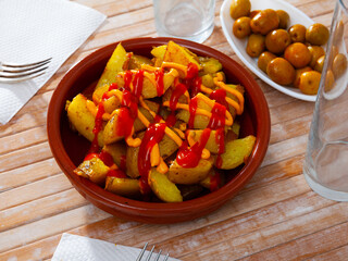 Traditional Spanish Patatas bravas, fried potatoes served with spicy sauce in clay bowl