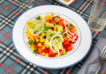 Popular all over the world appetizing vegetable salad of tomatoes, avocado, canned corn and onion, cut into rings
