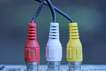 three colored old plugs with wires are connected to a electrical metal appliance on a gray...