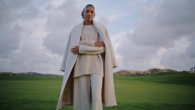 Stylish model posing field at cloudy sky. Serene black hair woman admiring green