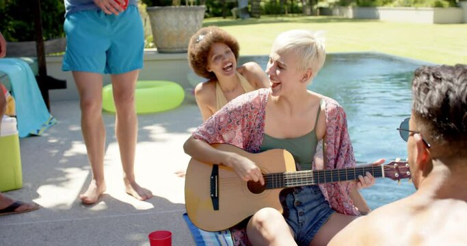 Happy diverse group of friends playing guitar at pool party in summer