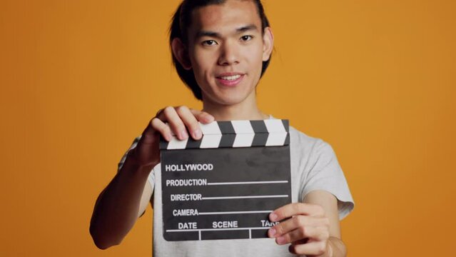 Excited carefree guy using film slate on camera, working in movie production industry with clapperboard. Male model being happy enjoying cinematography and cutting scene, having fun.