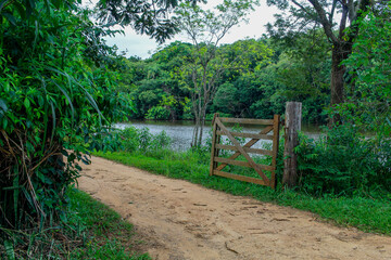 open wooden gate with a dirt road and a lake full of trees in the background