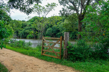 open wooden gate with a dirt road and a lake full of trees in the background