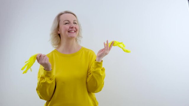 woman puts yellow latex gloves on her hands, beautiful, sexy woman, a housewife, in a white sweater and yellow gloves. High quality photo waving latex gloves