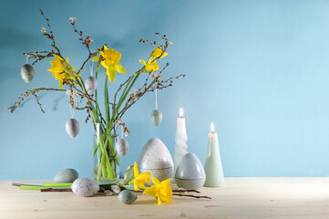 Seasonal holiday decoration with candles, a bouquet of daffodils and spring branches in a glass...