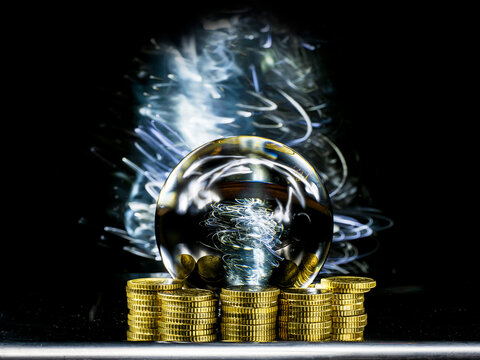 Crystal magical glass ball on stack of golden coins, abstract light painting on dark background. Forecasting money and profit gain. Financial sorcery. Foreseeing and predicting future economy turns