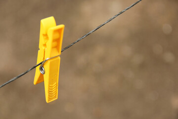 A yellow clean plastic cloth peg hanging on a wire - obrazy, fototapety, plakaty