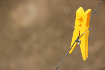 A yellow plastic clothes pin hanging on a wire - obrazy, fototapety, plakaty