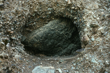 Beautiful nature background with big black stone in hole in mountain. Minimalist mountain landscape with large black boulder in dark rock hollow close-up. Atmospheric nature minimalism in mountains.