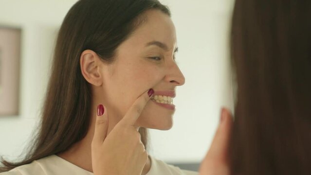 Woman checking her teeth in mirror with opened mouth looking for caries in bathroom at home. Teeth health care concept.
