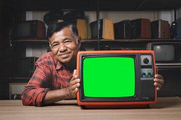 Smiling elderly man with red old TV with chroma green screen on wooden table in the room.