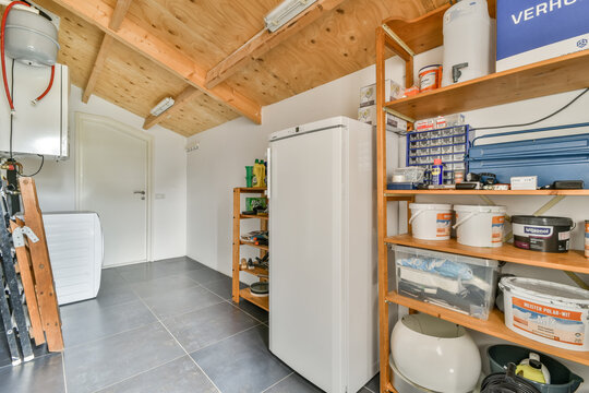 the inside of a garage with lots of tools and supplies on shelves, including a white refrigerator freezer in the corner