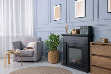 Black stylish fireplace near potted plant and armchair in cosy living room