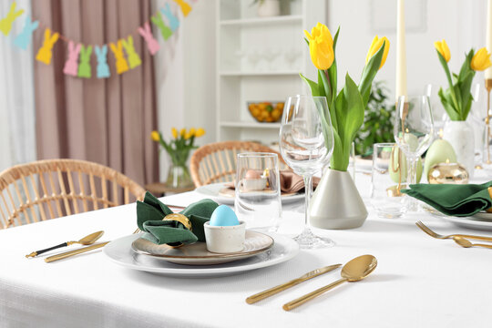 Festive Easter table setting with painted eggs, burning candles and yellow tulips in room