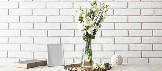 Vase with beautiful eustoma flowers on table near light brick wall
