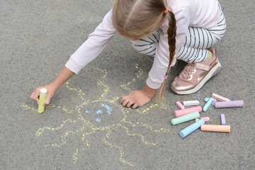 Little child drawing sun with chalk on asphalt