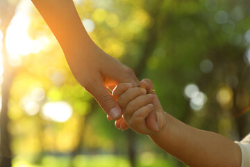 Daughter holding mother's hand outdoors, closeup. Happy family - obrazy, fototapety, plakaty