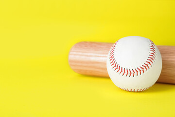 Wooden baseball bat and ball on yellow background, closeup. Space for text