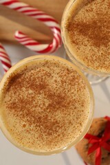 Tasty eggnog with cinnamon, cookies and candy canes on white table, flat lay