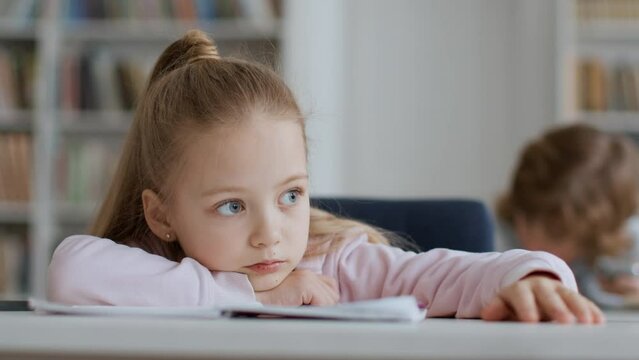 Bad mood at school. Upset little girl feeling boring during lessons, lying on desk and tapping fingers, free space