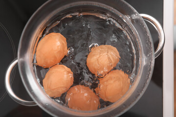 Glass cooking pot with boiling eggs on stove in kitchen, closeup